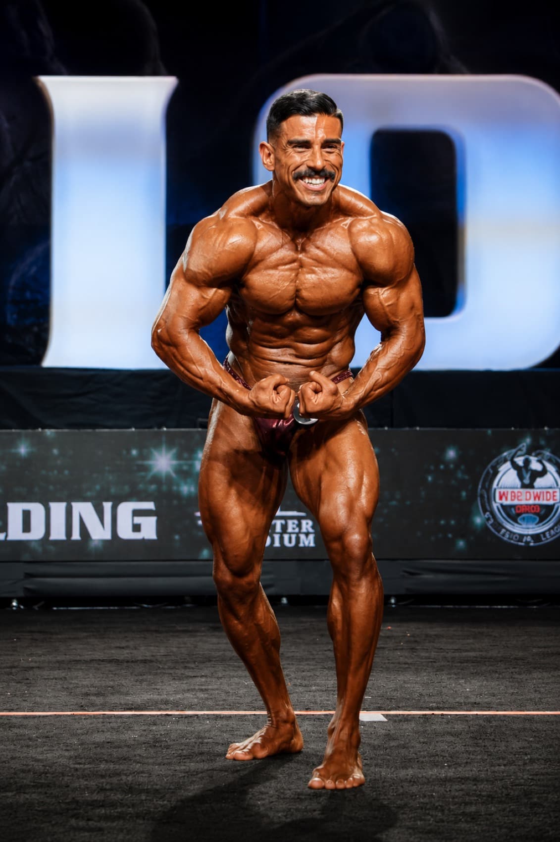 Christian Burrola competing on stage at a bodybuilding show